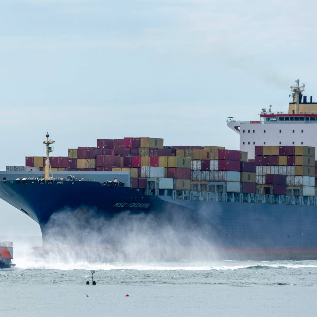 Large cargo ship loaded with containers sailing through water.