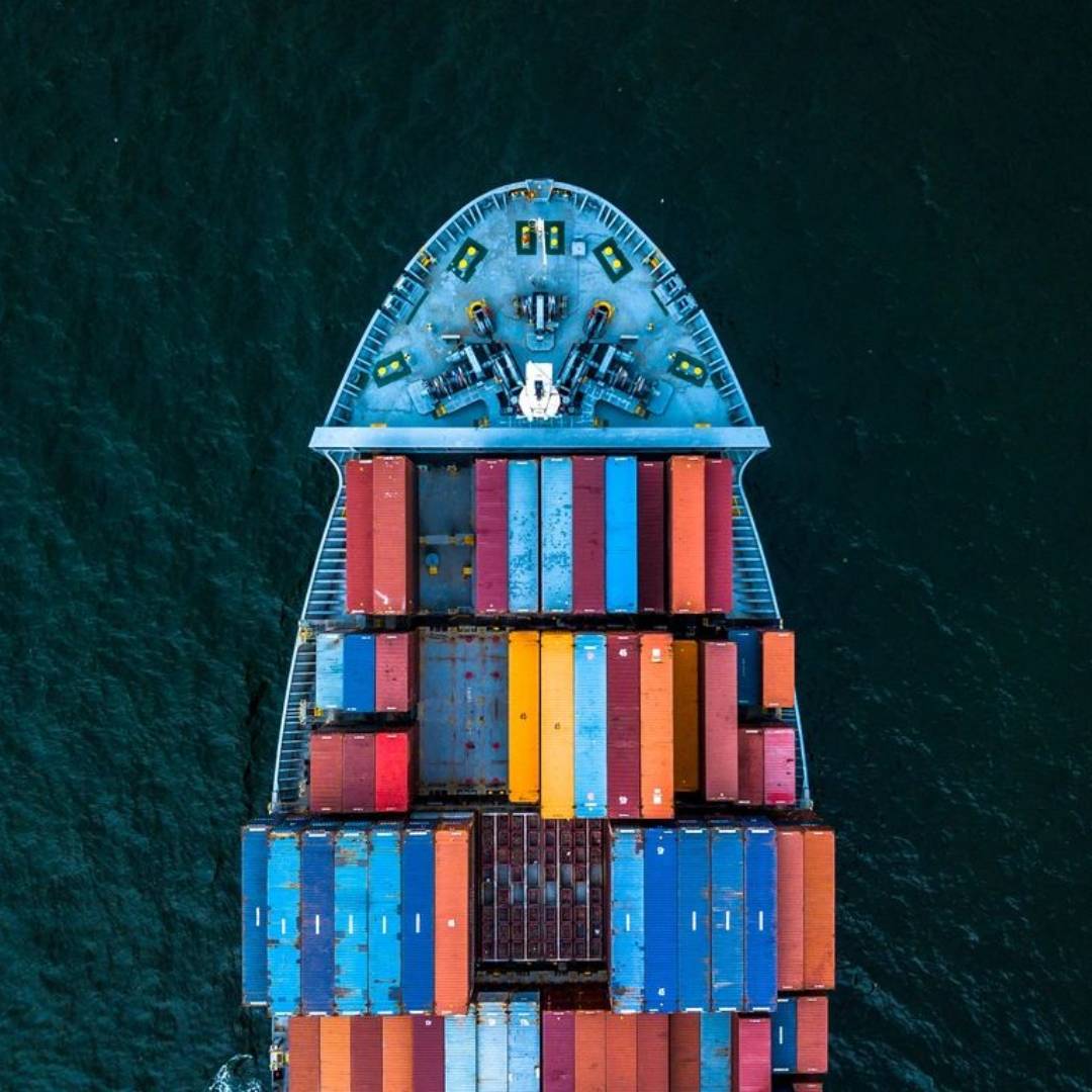 A top-down view of a cargo ship loaded with colorful containers sailing in dark water.